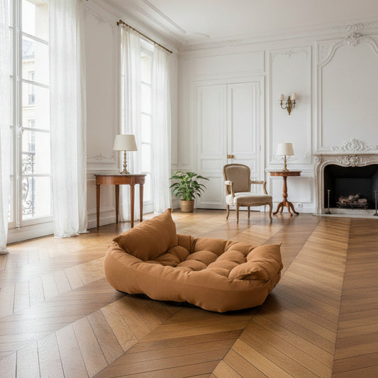 Coussin moelleux cognac dans un salon haussmannien avec parquet en chevrons et hautes fenêtres — intérieur élégant avec animal