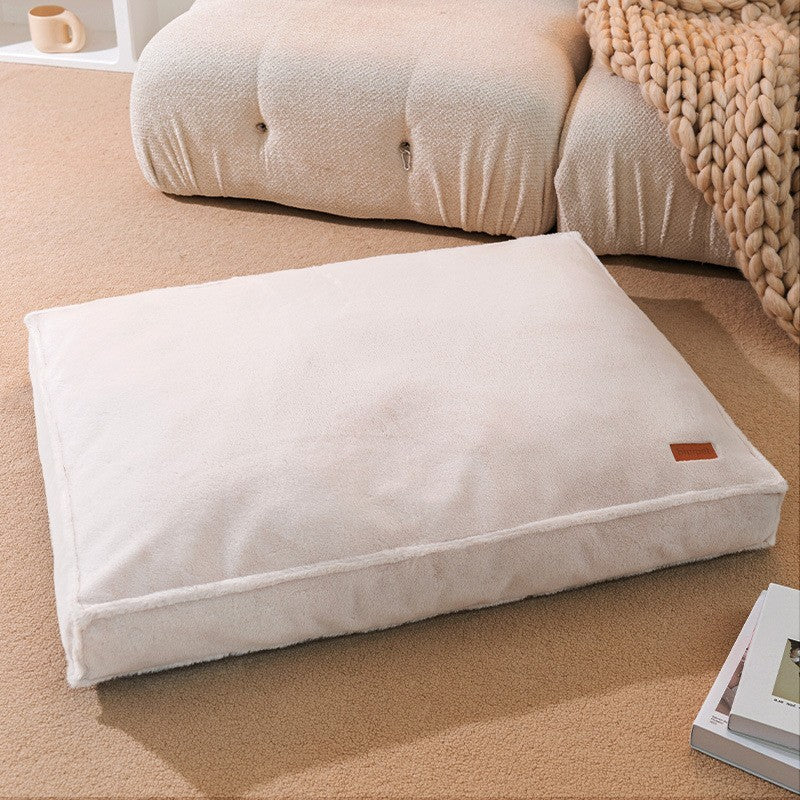 Matelas plat ivoire pour chien posé sur tapis beige dans un salon cosy avec plaid en laine tressée — coussin imperméable lavable design
